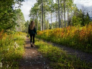 woman in black jacket walking on pathway between green grass and trees during daytime